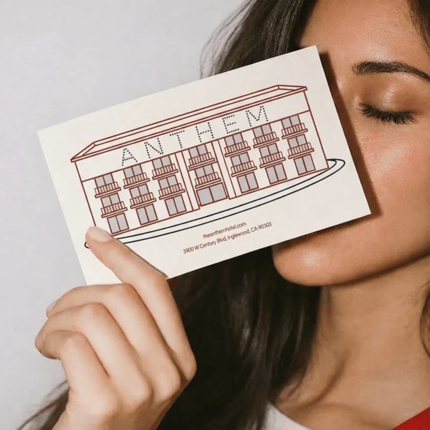 A woman holding a postcard up to her face, eyes closed, the postcard has an illustration of the Anthem hotel on the front