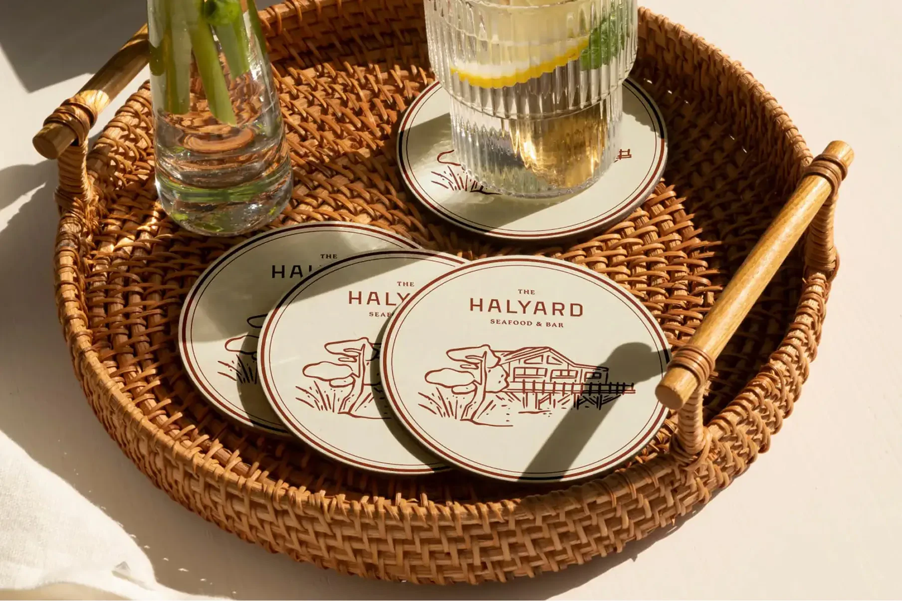 Round Halyard coasters in woven tray beside drinking glasses
