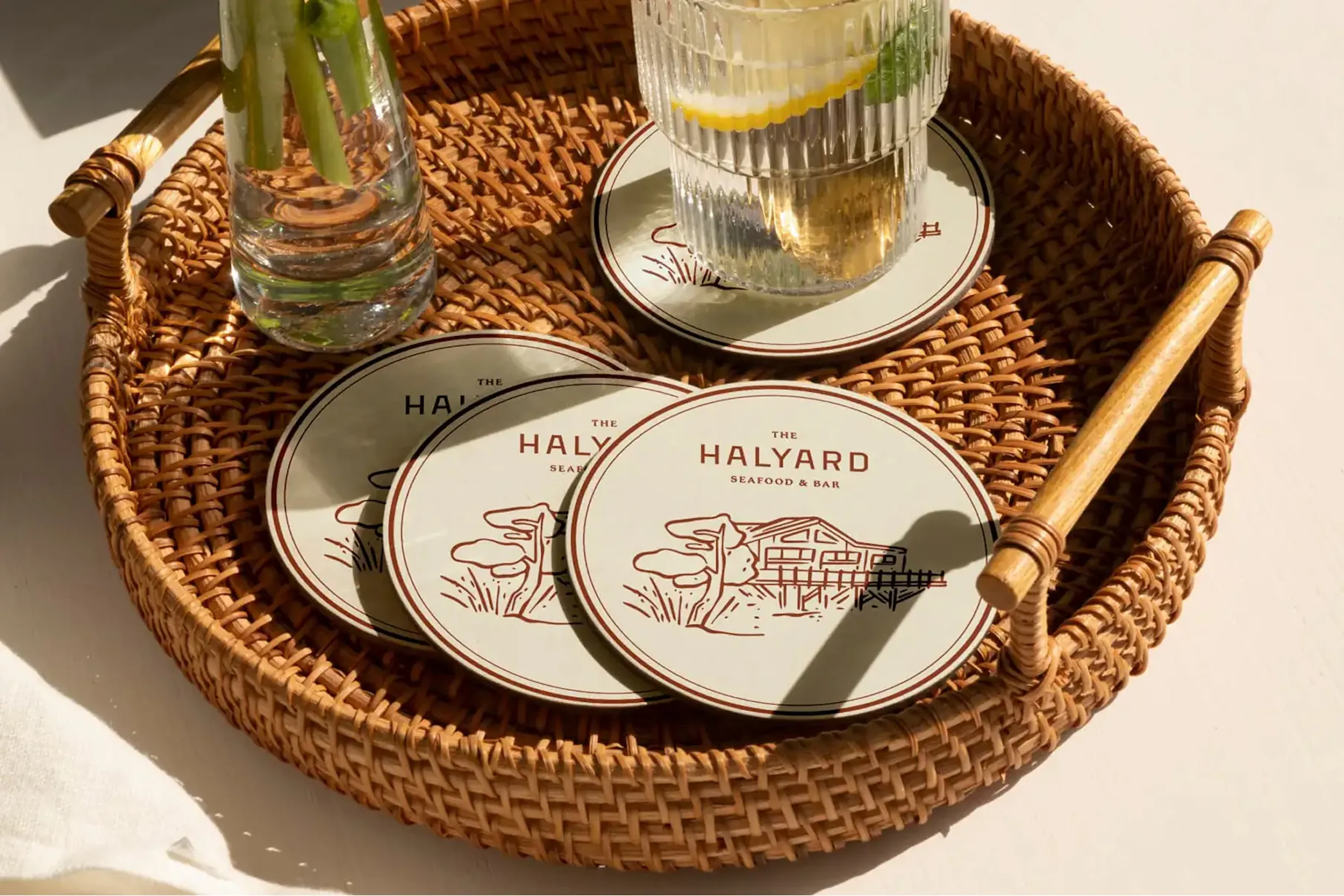 Round Halyard coasters in woven tray beside drinking glasses