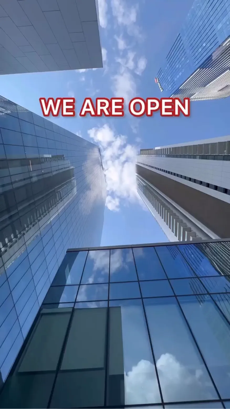 Upward view of skyscrapers with 'We Are Open' text overlay