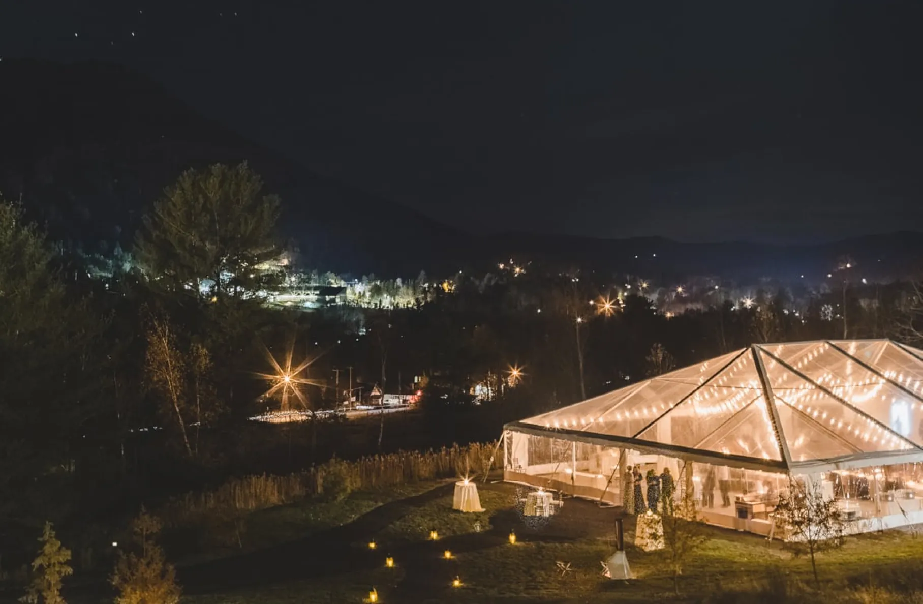 Aerial night view of a lit event tent by a lake