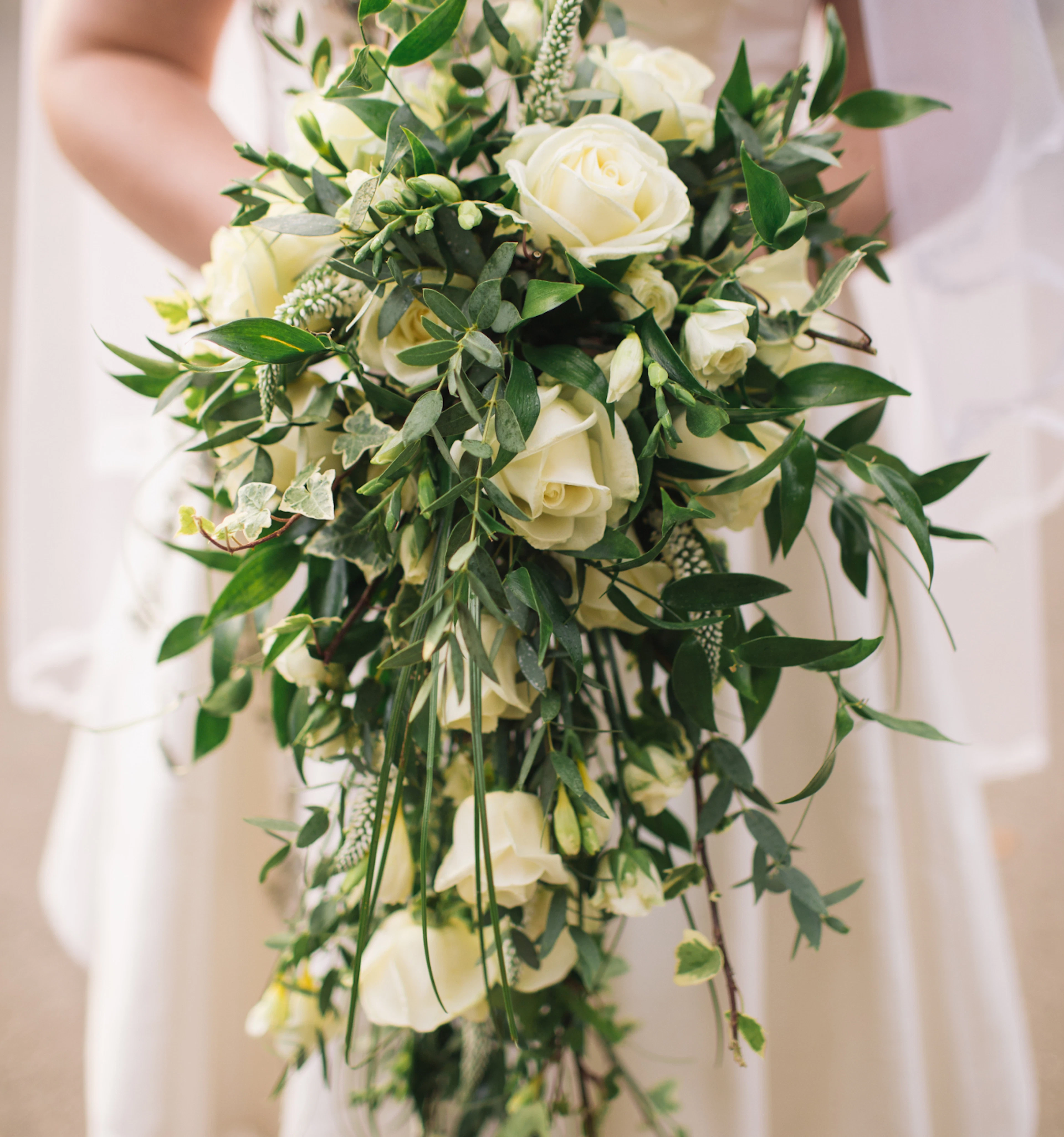 Woman in a wedding dress holding a beautiful flowing bouquet of white roses and greenery