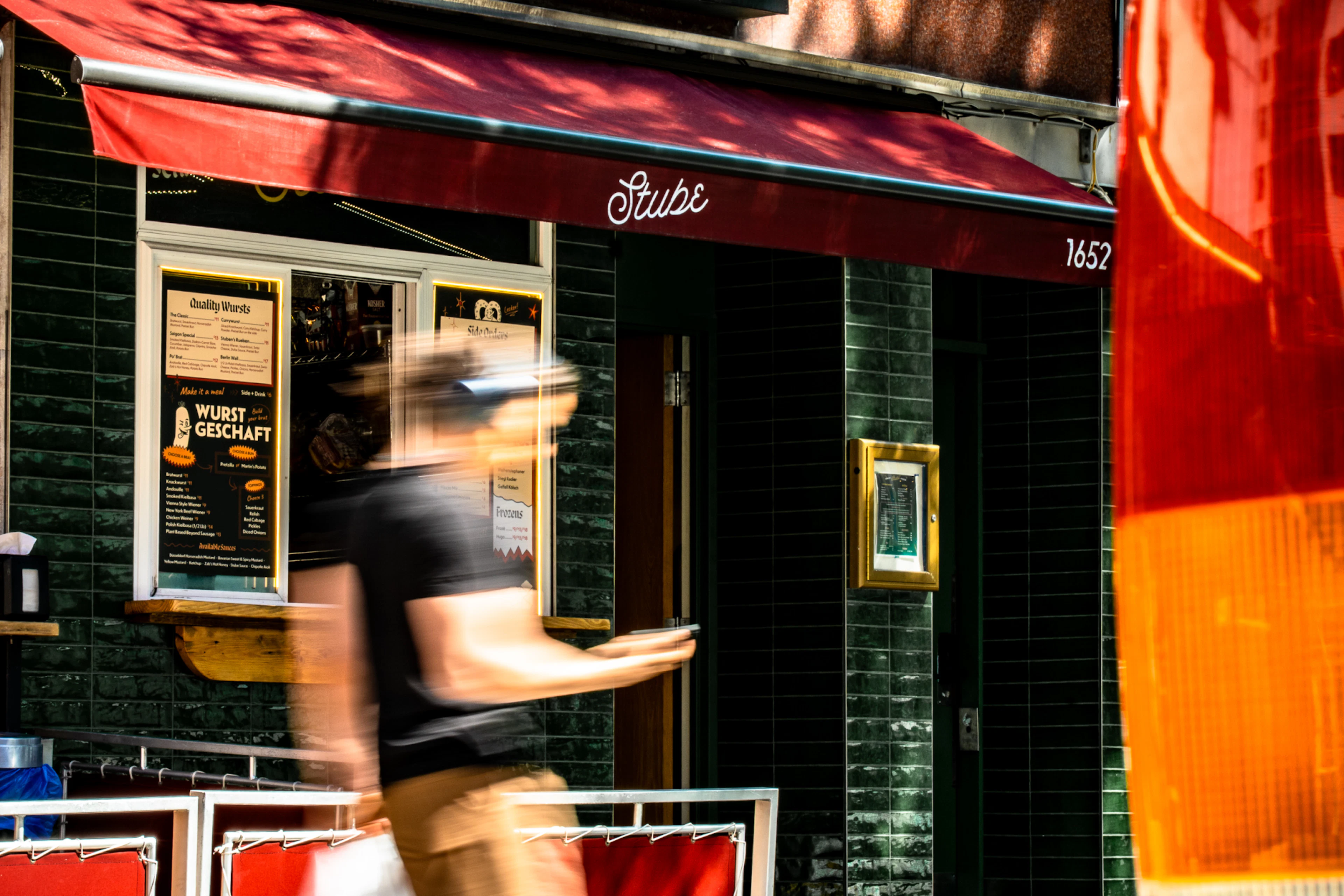 Man walking down the street in front of the Stube, he's motion blurred and it's a sunny day in NYC