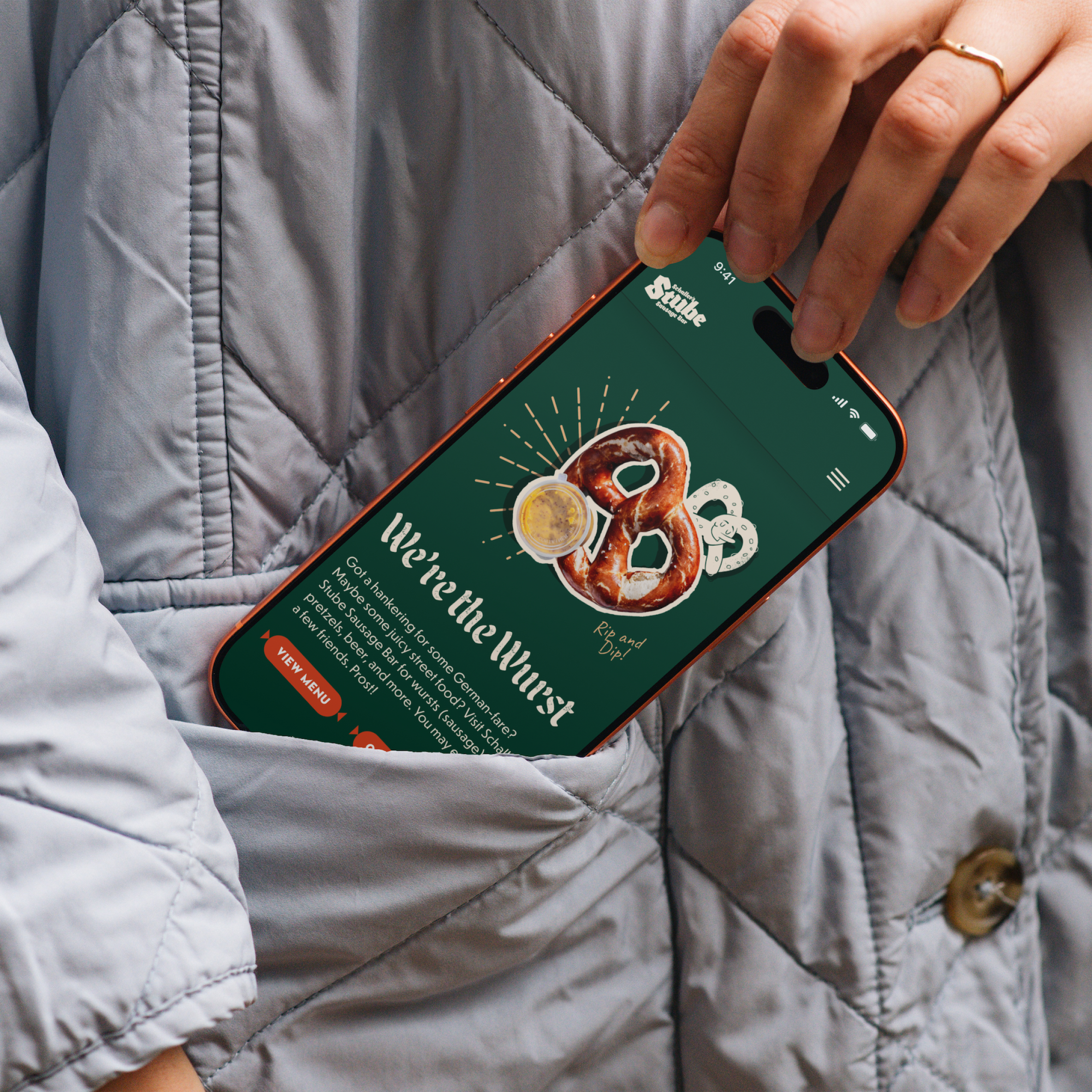 A close up image of a woman pulling a cellphone out of her jacket pocket with the Stube website on the screen