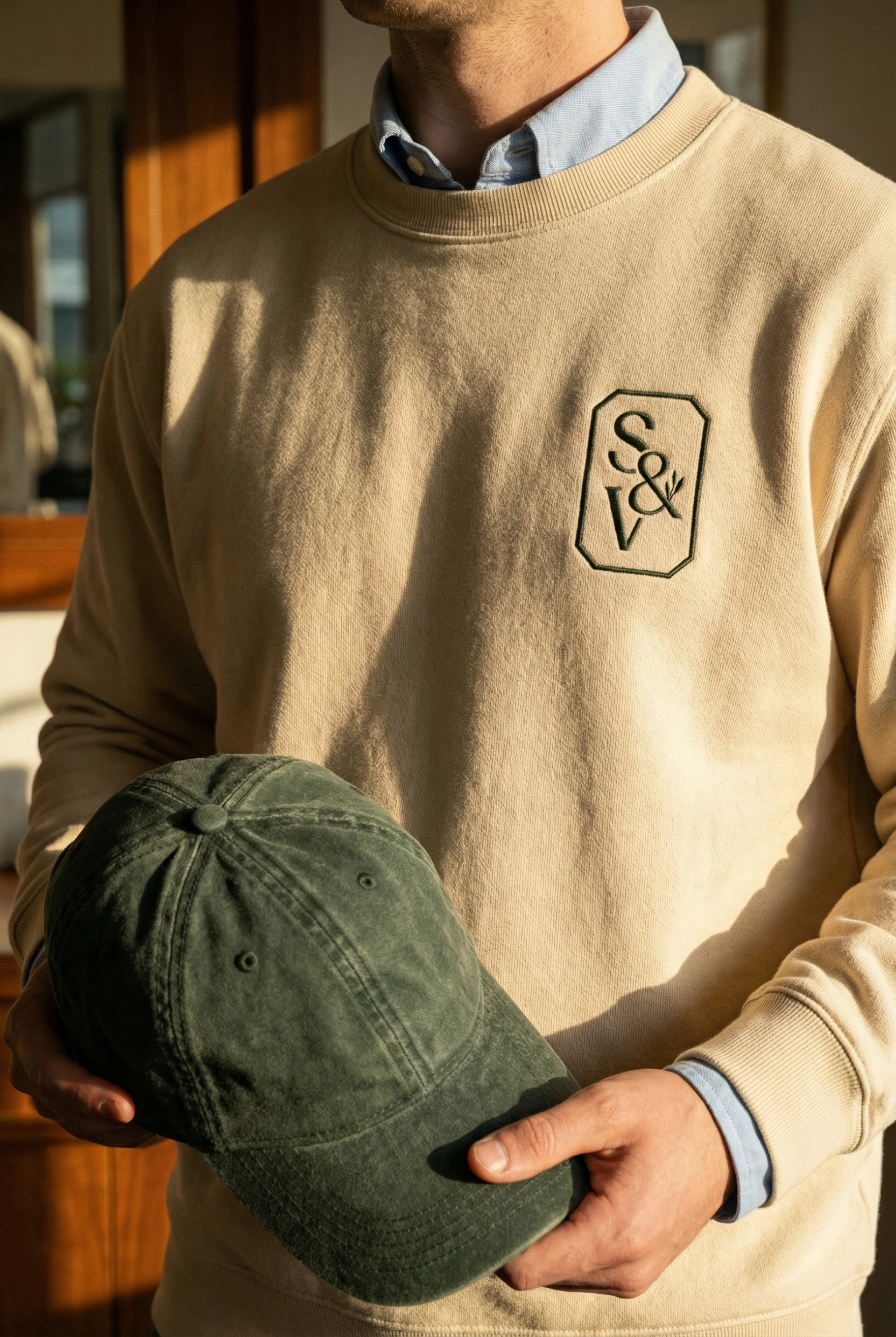 Man in embroidered sweatshirt holding green cap