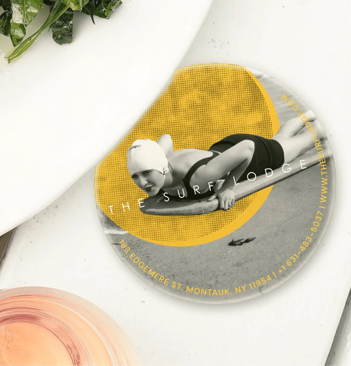 The Surf Lodge branded coaster with a vintage swimmer photo, on a table