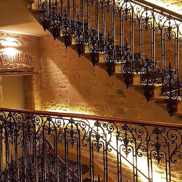 Intérieur de l'hôtel, escalier avec garde de corps, mur de pierre et éclairage qui longe le mur.