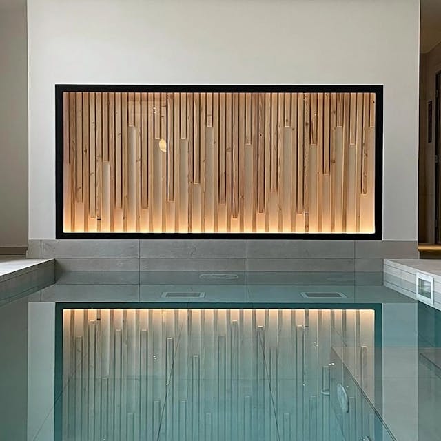 Vue sur le spa avec piscine en premier plan et mur fait de tasseau de bois éclairé avec une led rasante en contre plongée 