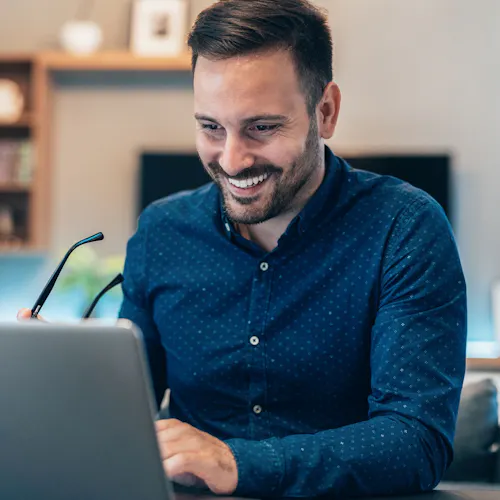 uomo che sorride davanti a pc con occhiali in mano uomo che sorride davanti a pc con occhiali in mano