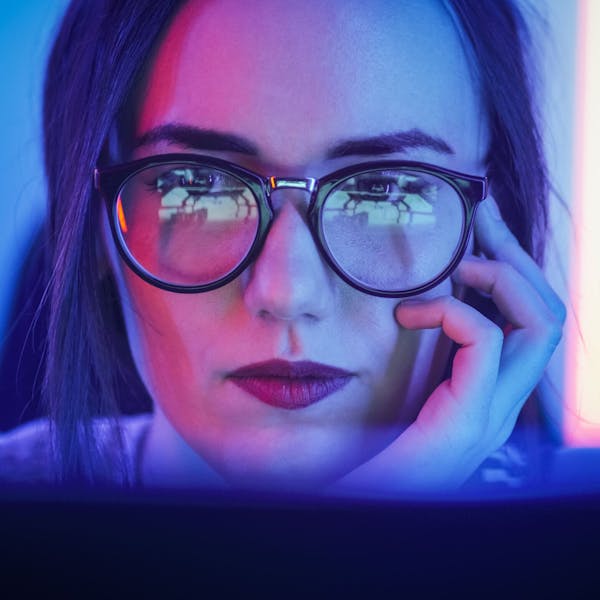 Une femme qui porte des lunettes regarde attentivement son écran d'ordinateur