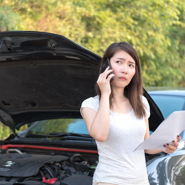 Jeune femme au téléphone devant sa voiture en panne