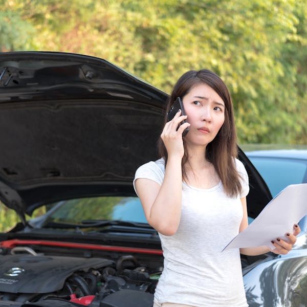 jeune femme au téléphone devant sa voiture en panne