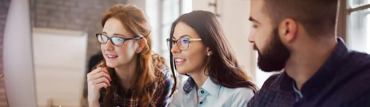 présentation de travail : deux femmes et un homme devant un grand écran d'ordinateur