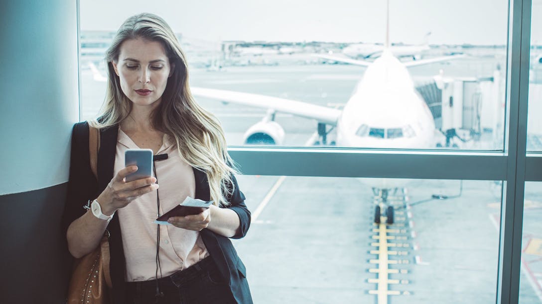 Femme qui consulte son téléphone portable devant le tarmac d'un aréroport