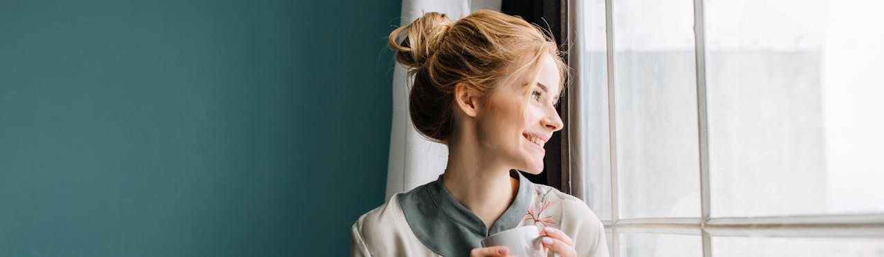 Donna che sorride girata a guardare fuori dalla finestra