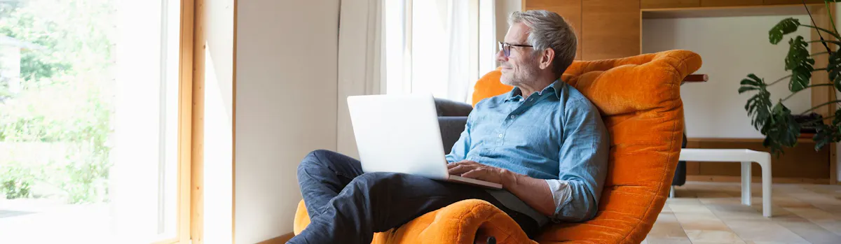 homme assis dans un fauteuil orange avec son ordinateur sur les genoux homme assis dans un fauteuil orange avec son ordinateur sur les genoux