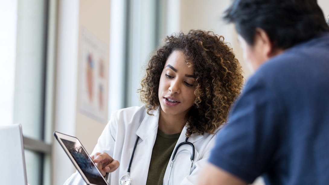 Médecin en blouse blanche en consultation avec son patient et une tablette