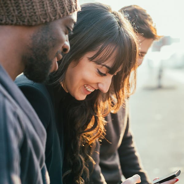 Femme entourée de deux hommes consulte son smartphone en riant