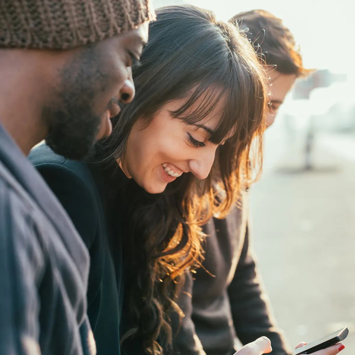 femme entourée de deux hommes consulte son smartphone en riant femme entourée de deux hommes consulte son smartphone en riant