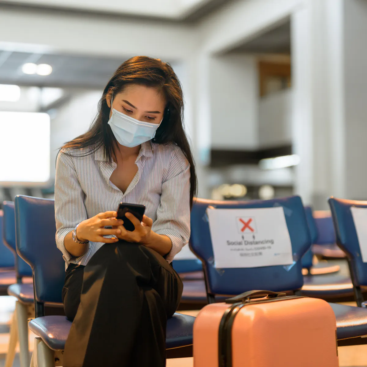 femme qui consulte son mobile avec sa valise dans la salle d'attente d'un aéroport