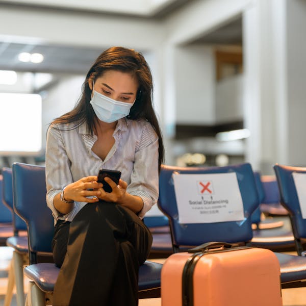Femme qui consulte son mobile avec sa valise dans la salle d'attente d'un aéroport