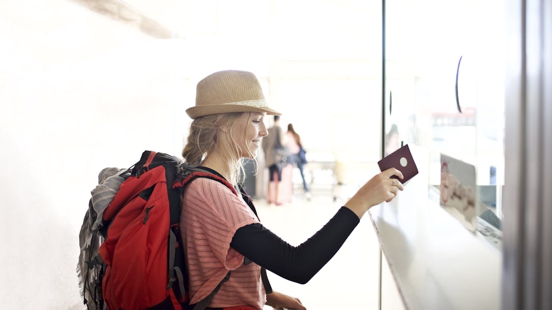Voyageuse avec un sac à dos, un chapeau de paille et un passeport à la main devant un tableau d'informations