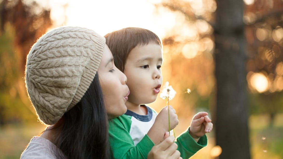 woman with boy breathe on a flower