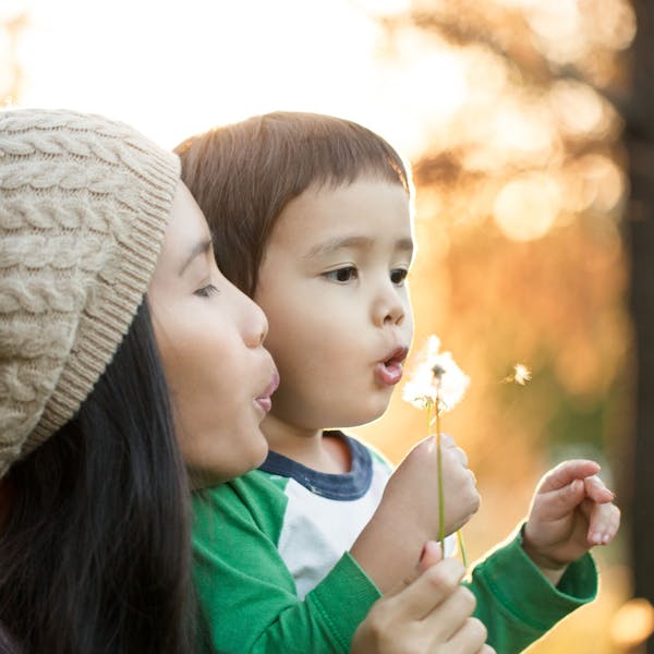 woman with boy breathe on a flower