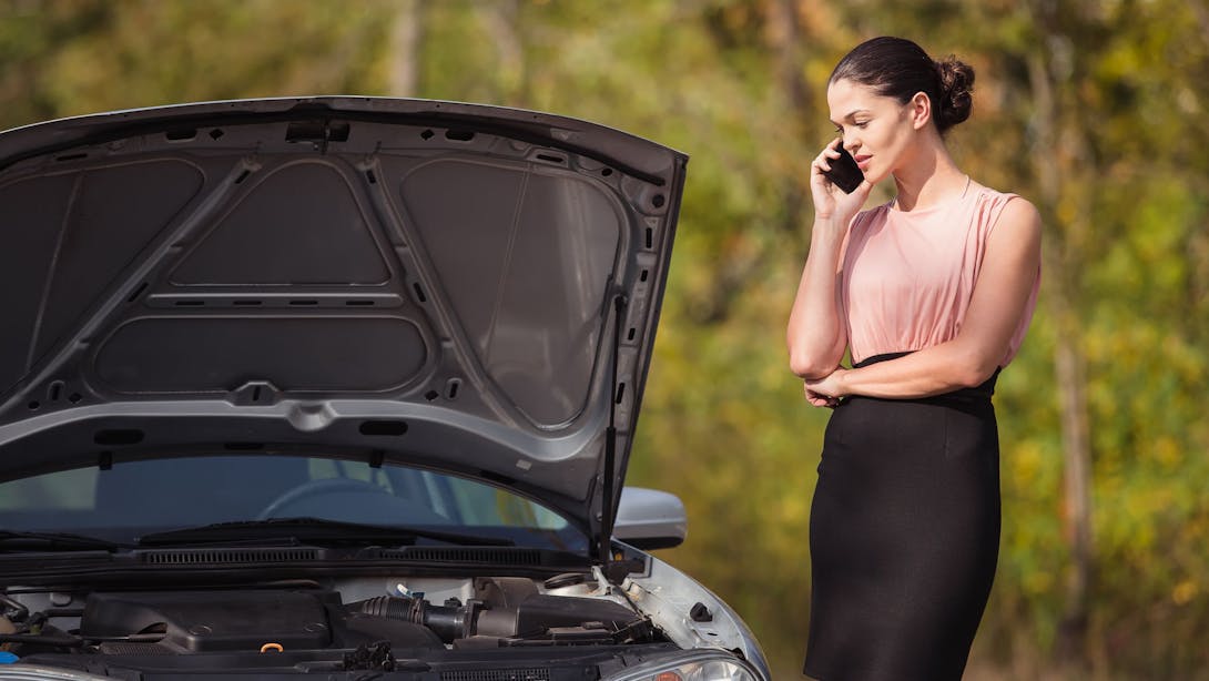 Une femme contacte l’assistance devant sa voiture en panne avec son téléphone mobile
