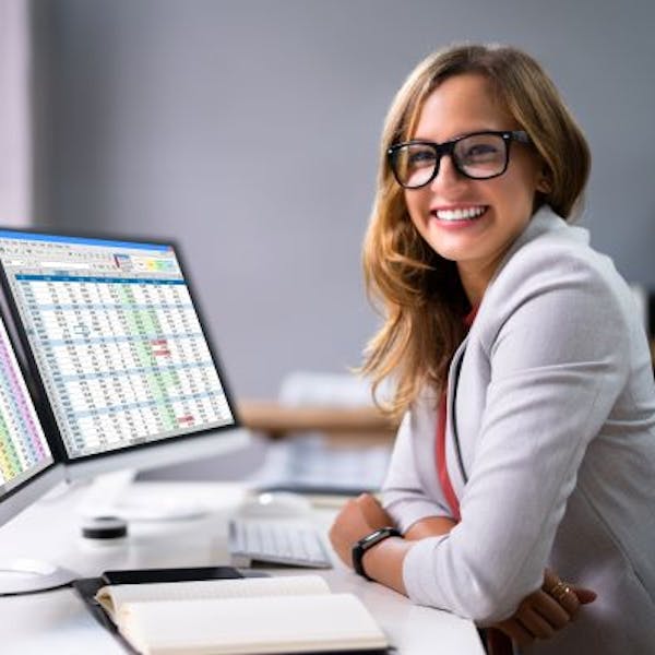 A woman smiles at an Excel spreadsheet and an open notebook