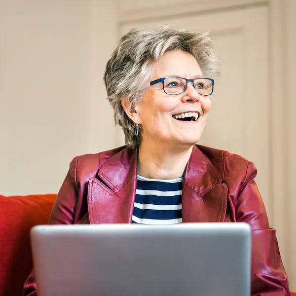 A woman with blue glasses smiles at her laptop screen