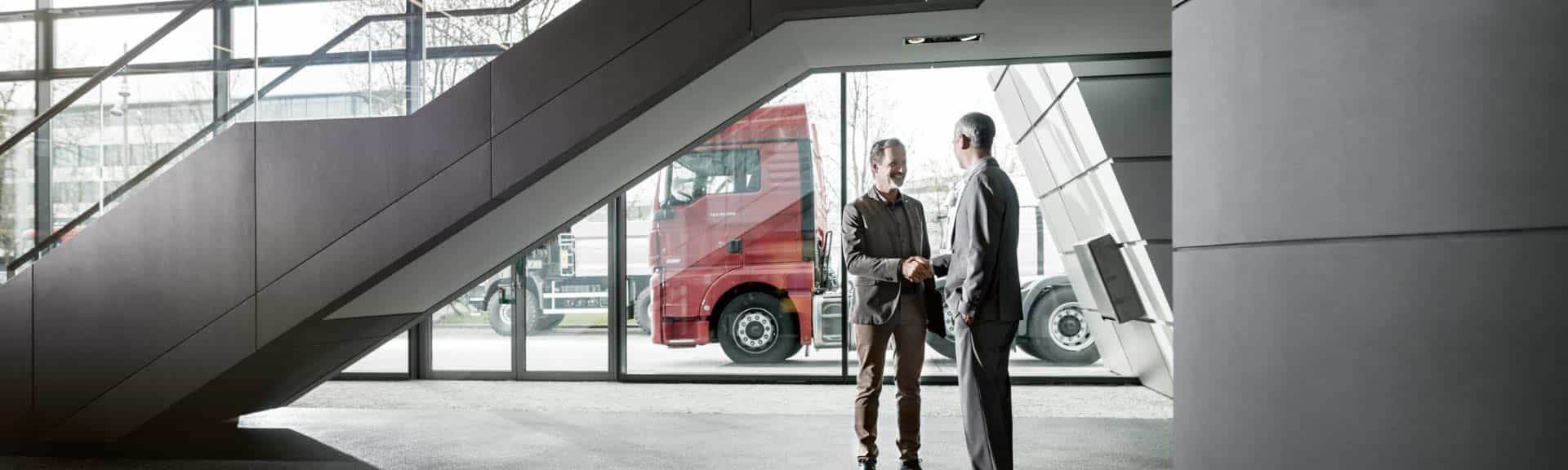 Dos hombres se dan la mano delante de dos vehículos pesados