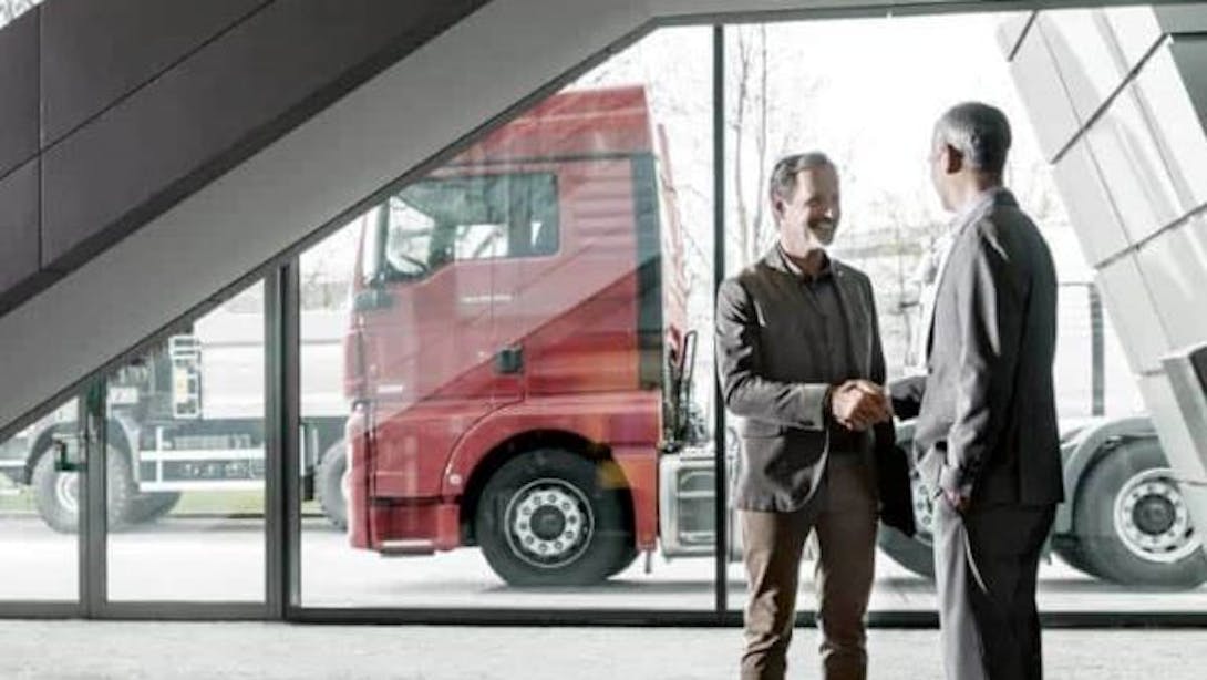 Two men shake hands in front of two heavy goods vehicles