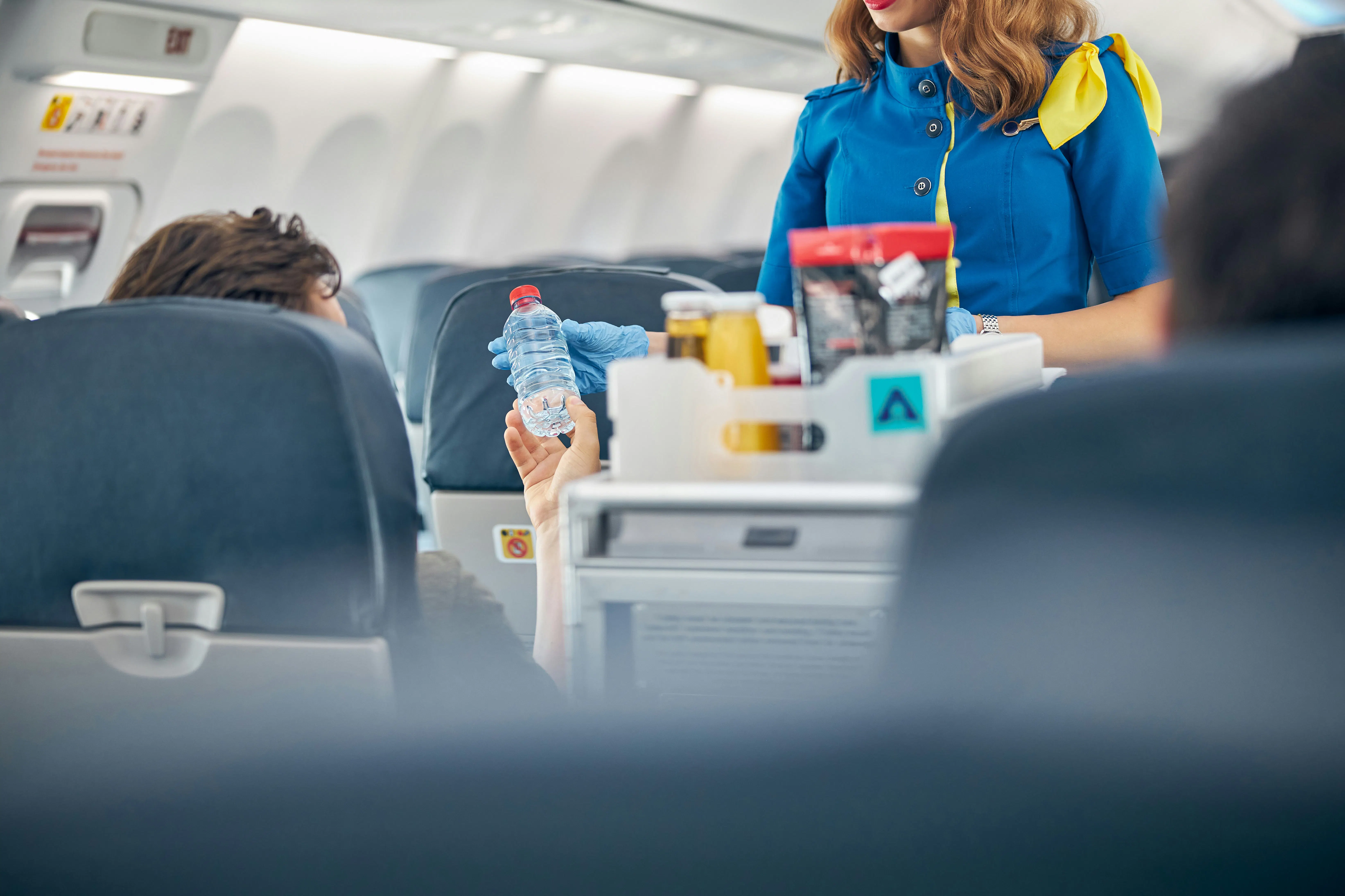 Air stewardess passes water bottle to seated customer on plane