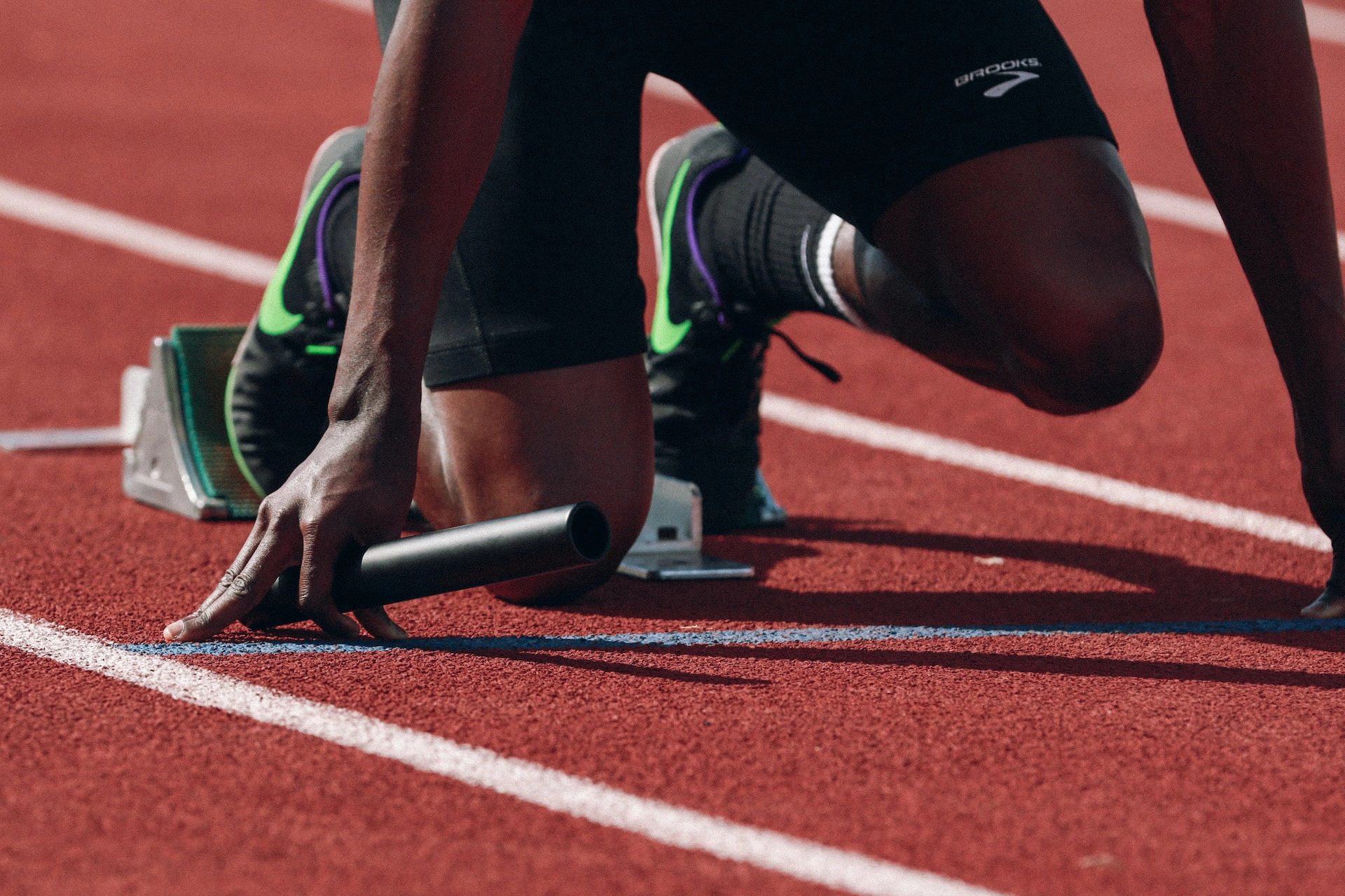 A relay race runner sets at a track starting block while holding a baton