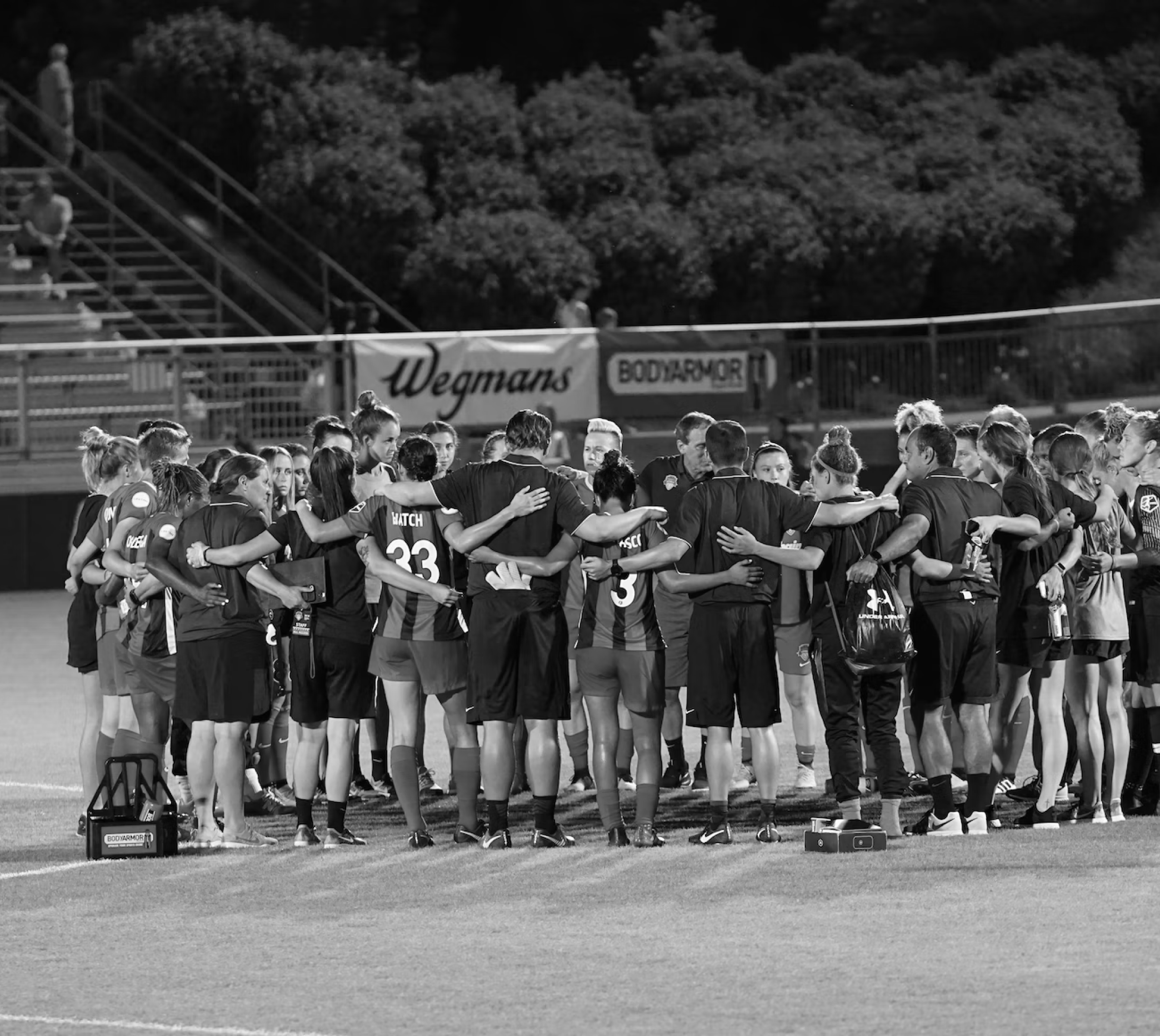 A team of youth football players and their coach huddle up with arms around each other on a soccer field