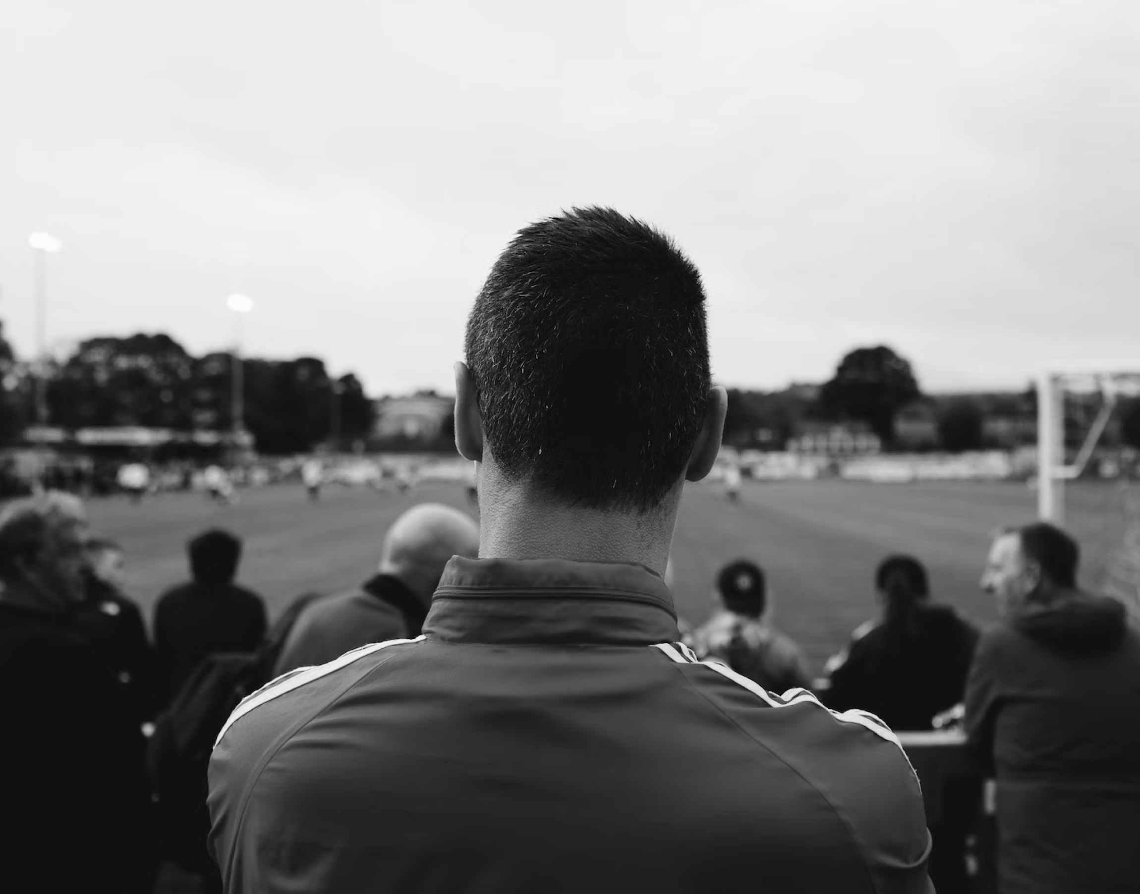 La cabeza de un líder de club visto desde atrás, observando un campo de juego desde la banda