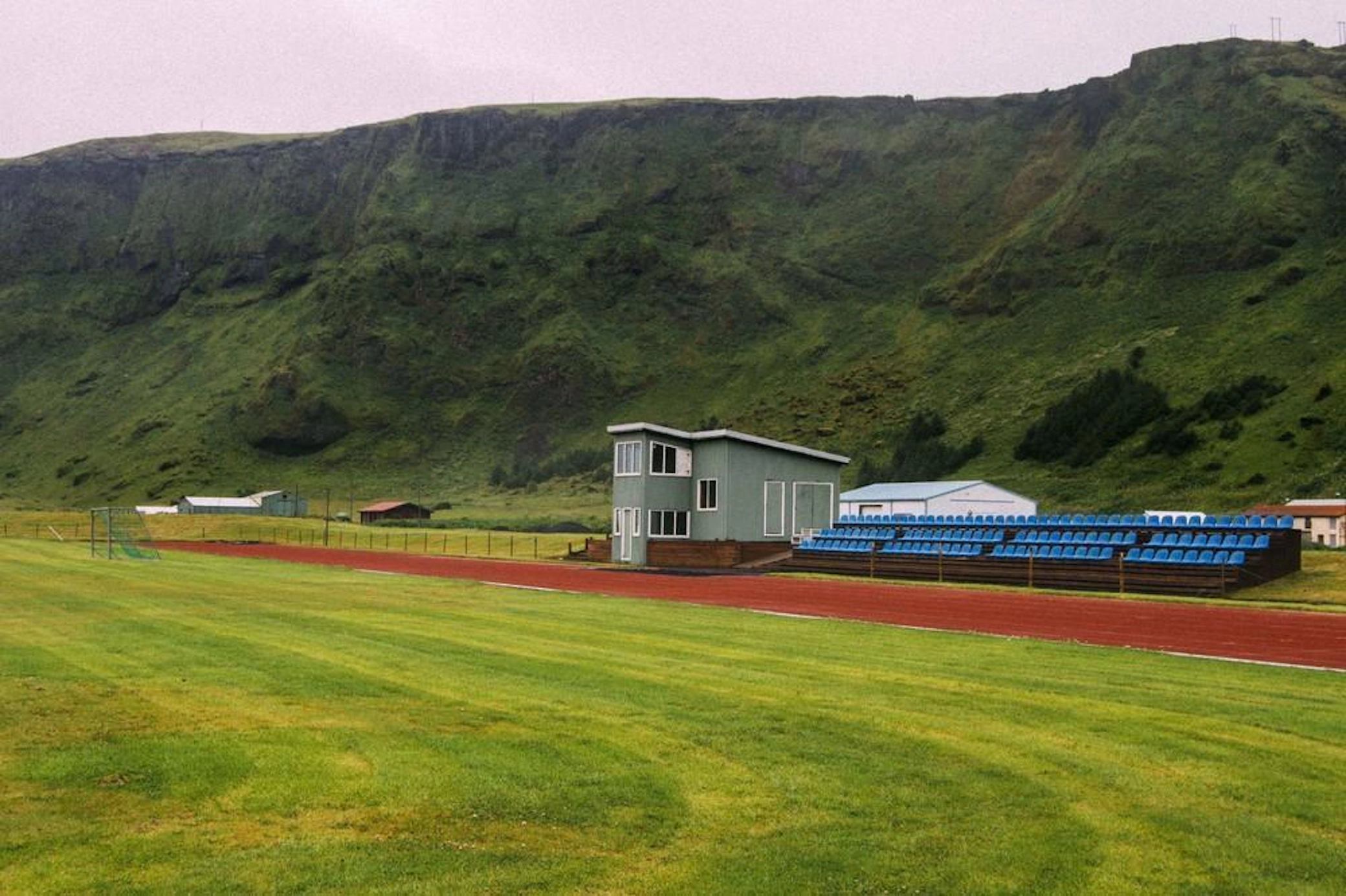 Rural sports facility with running track and blue bleachers against green hillside backdrop