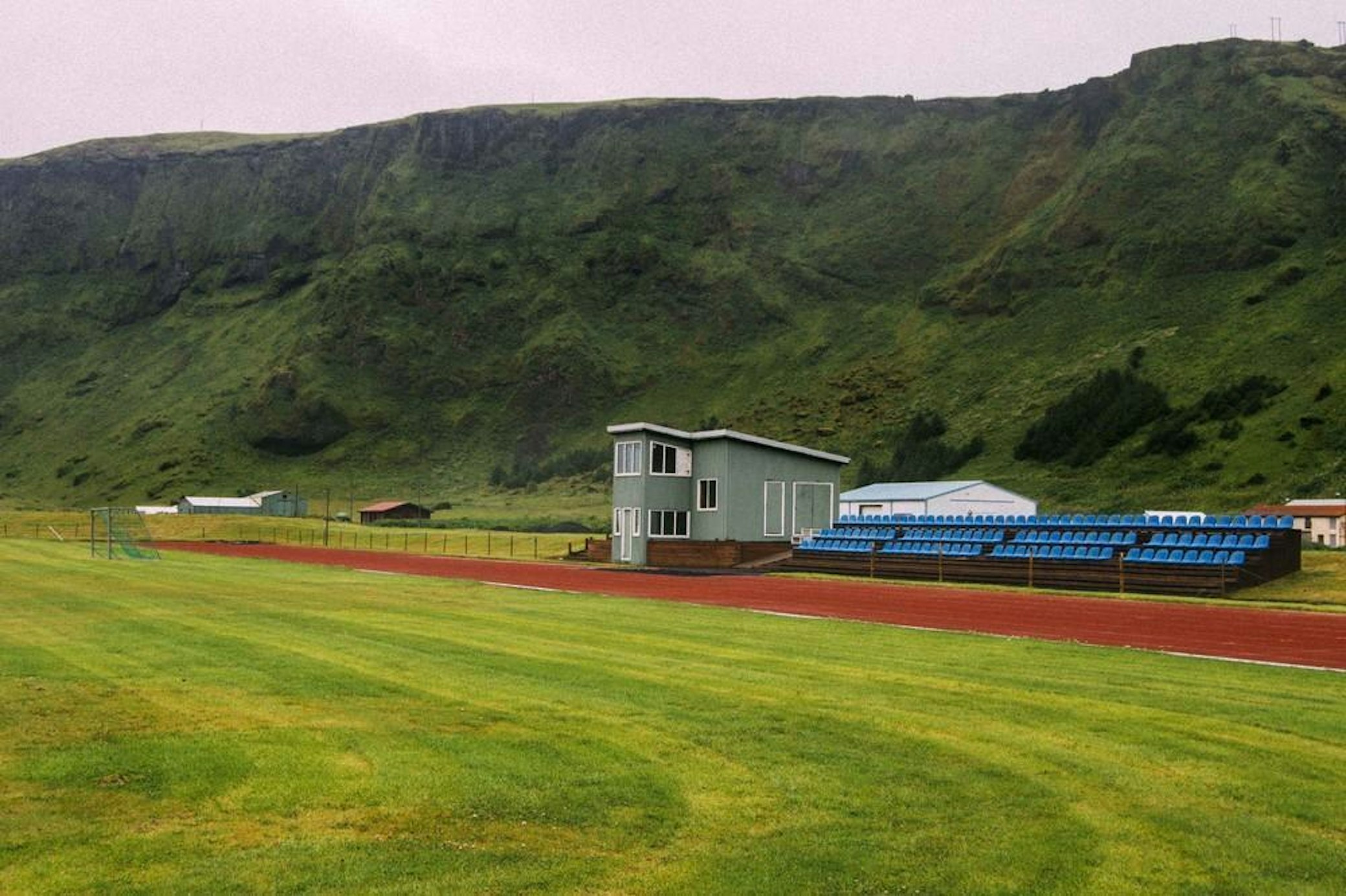 Rural sports facility with running track and blue bleachers against green hillside backdrop
