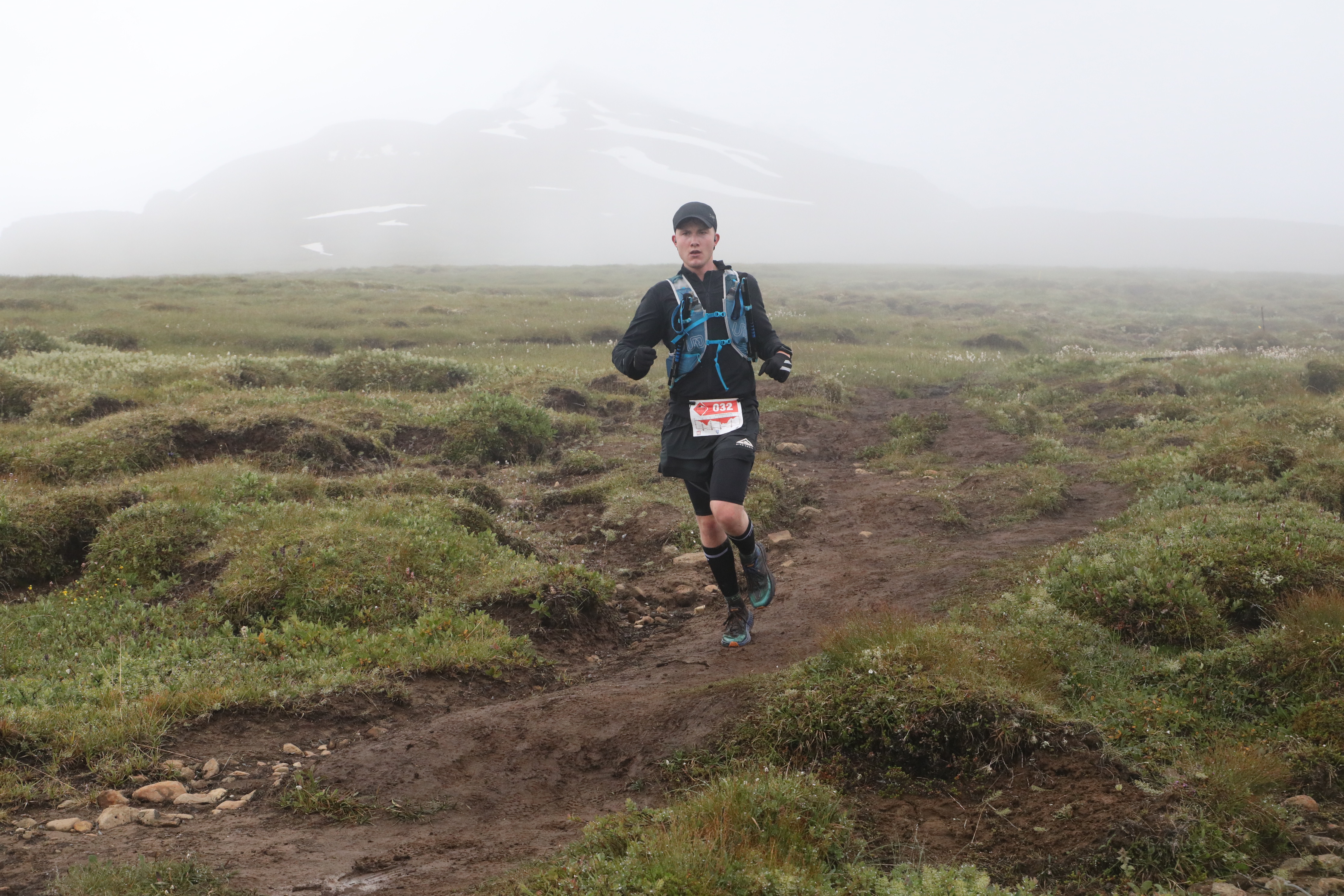 Ultra marathon runner competing on misty mountain trail in challenging terrain and weather conditions