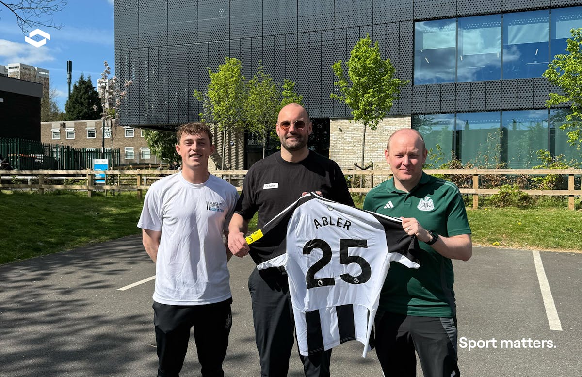 Three men holding a Newcastle United jersey with "ABLER 25" printed on the back.