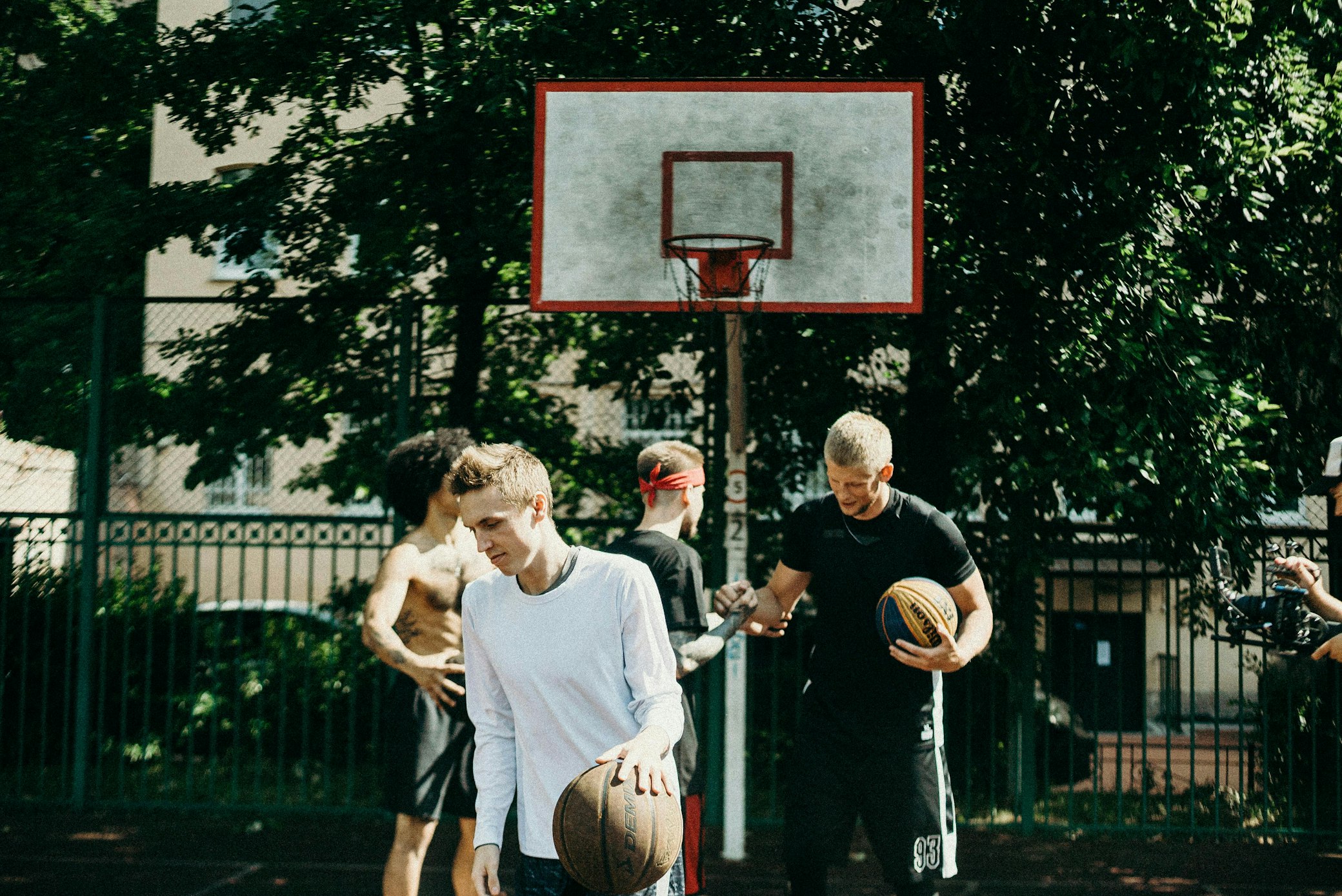 Jóvenes jugando baloncesto en cancha exterior con aro y vegetación de fondo