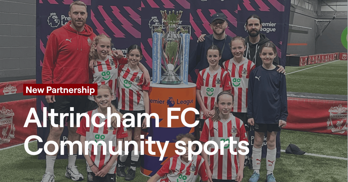 Group of children and adults posing with a football trophy, celebrating a new partnership.