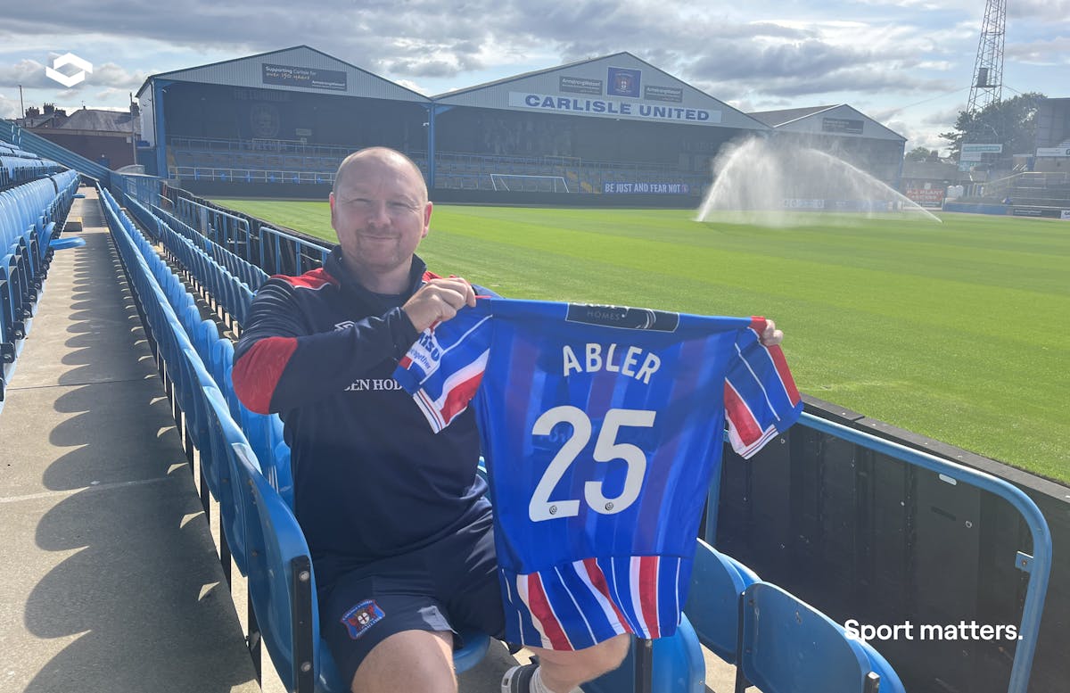 A smiling man in a stadium holding a football jersey with the Abler logo and number 25.