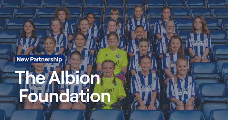 Young female football players from The Albion Foundation's programmes wearing West Bromwich Albion striped jerseys, posing together at The Hawthorns stadium, representing the Foundation's commitment to youth development and community engagement.