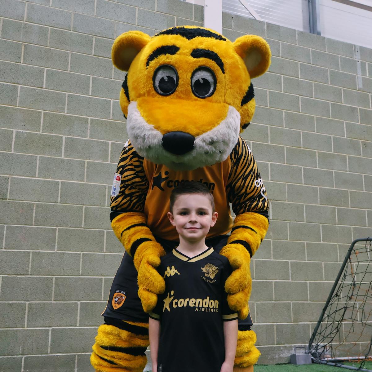 Hull City AFC mascot with young supporter in Tigers jersey celebrating community partnership at football stadium