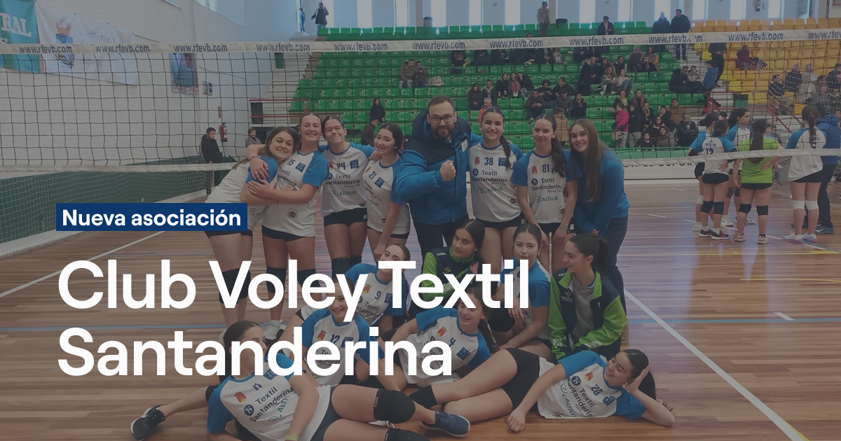 Equipo femenino del Club Voley Textil Santanderina posando en grupo en la cancha con sus entrenadoras, vistiendo uniformes blancos y azules, con gradas verdes y amarillas al fondo