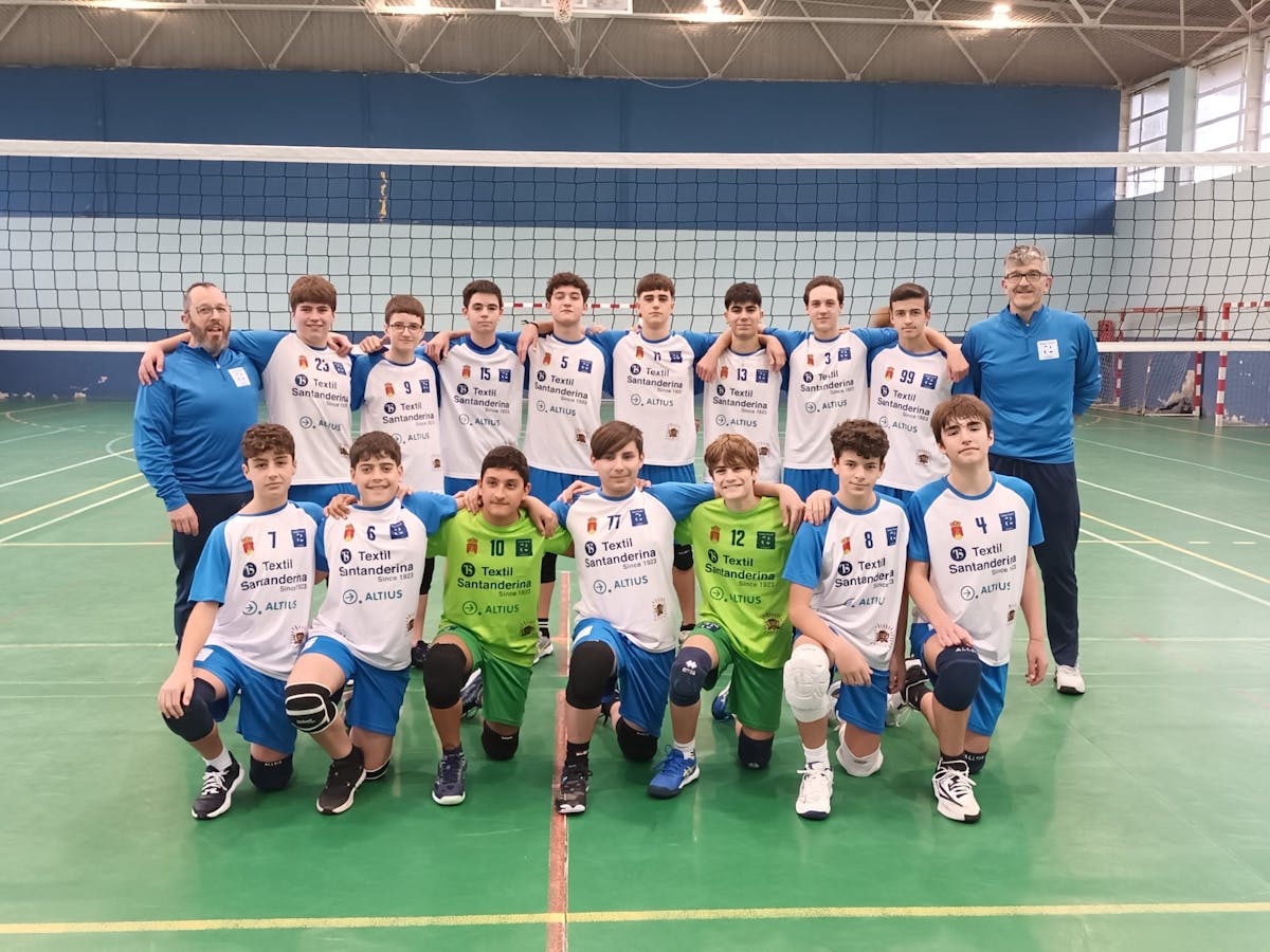 Equipo masculino juvenil del Club Voley Textil Santanderina posando en formación con sus entrenadores, vistiendo uniformes blancos y azules con patrocinadores, en cancha de voleibol cubierta