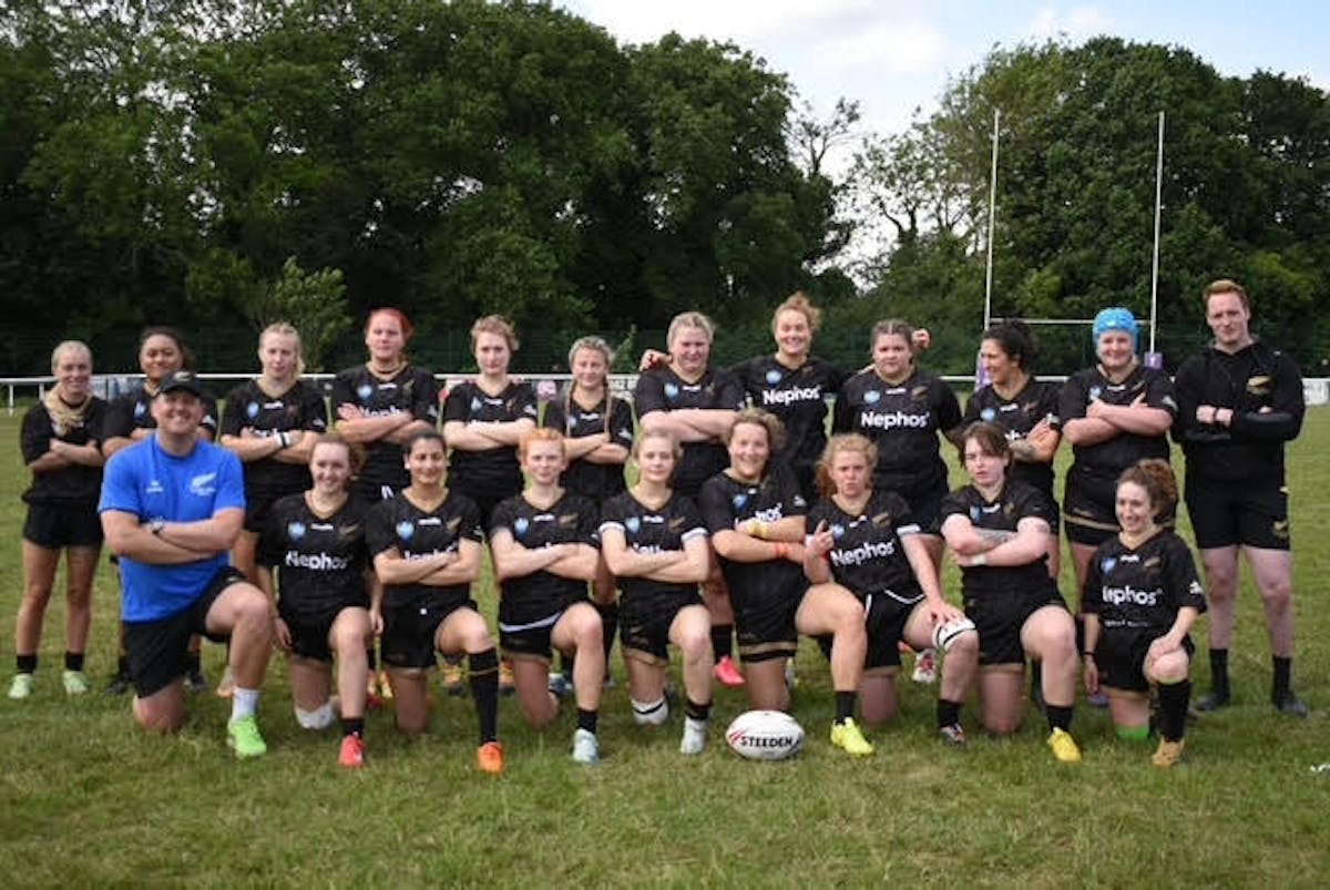 All Golds women's rugby league team, the Bristol Golden Ferns, posed together on a grass pitch. Approximately 15 players wearing black Nephos-sponsored jerseys are arranged in two rows with coaches and staff, surrounded by trees in the background.