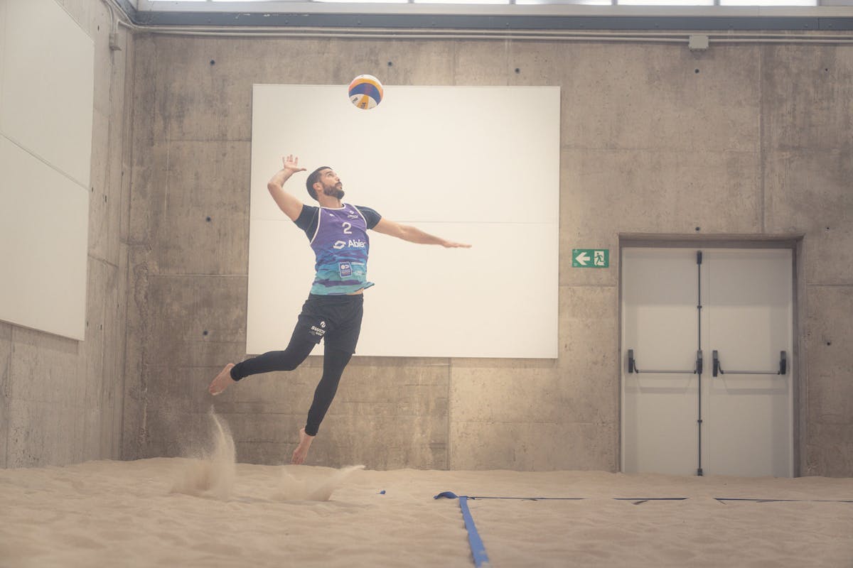 Switch Volley player jumping to spike the ball on indoor beach volleyball court wearing Abler-branded uniform